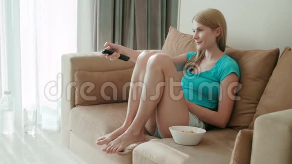 美丽迷人的女人坐在沙发上看电影吃白碗里的薯片视频的预览图