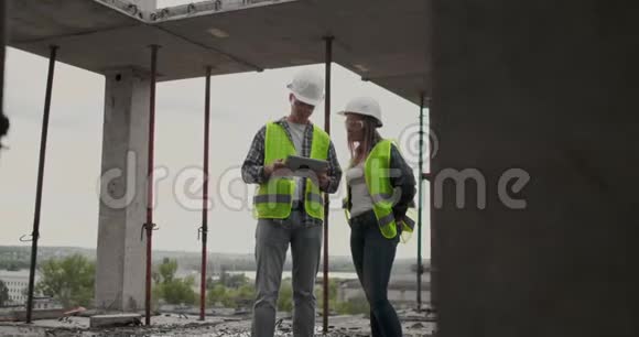 两名工程师一男一女在一个建筑工地上拿着一台平板电脑谴责项建筑计划视频的预览图