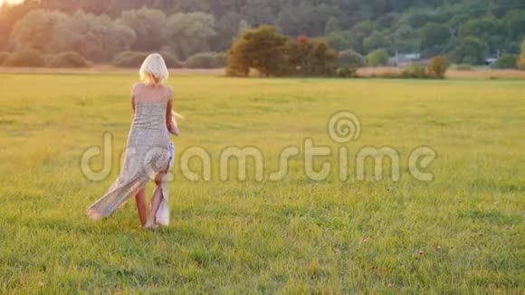 妈妈和她的女儿一起玩绕着她转在日落时美丽的草地上积极的生活方式视频的预览图