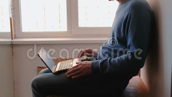 在笔记本电脑上工作一个面目全非的年轻人打开笔记本电脑等待它启动和输入坐在上面的东西视频的预览图