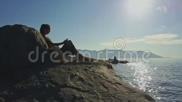 石头上的女孩听音乐对抗海洋视频的预览图