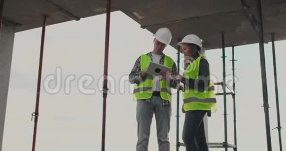 两名工程师一男一女在一个建筑工地上拿着一台平板电脑谴责项建筑计划视频的预览图