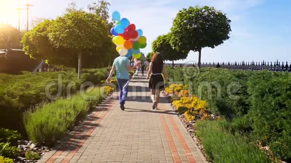 一对年轻夫妇带着一群五颜六色的气球在公园散步的慢动作视频视频的预览图