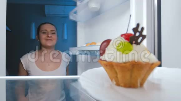 年轻女子偷偷地从冰箱里拿蛋糕的4K镜头有人阻止她视频的预览图