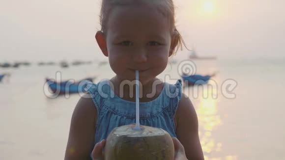 小女孩在日落时慢慢地在海边喝椰子水视频的预览图