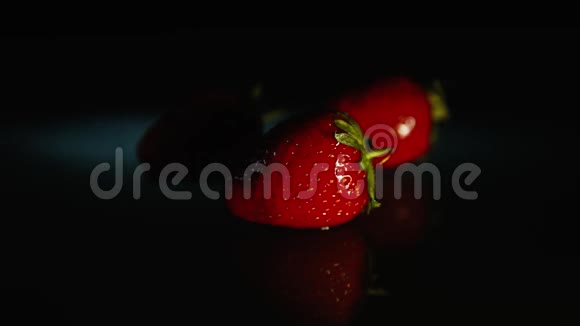 三个草莓躺在黑暗的桌子上黑色的背景在灯光下高清高清视频的预览图