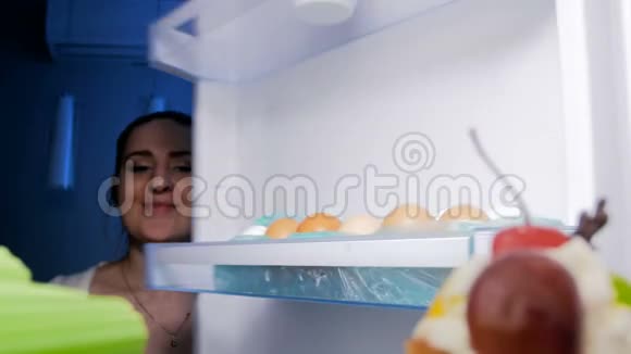4K镜头年轻微笑的女人晚上在冰箱里看着拿出芹菜视频的预览图