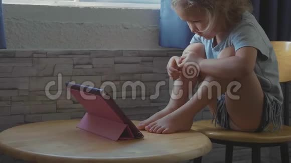 小可爱的小女孩坐在桌子旁看着平板电脑里的东西视频的预览图