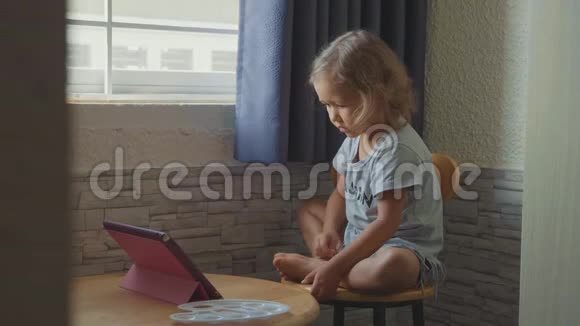 小可爱的小女孩坐在桌子旁看着平板电脑里的东西视频的预览图