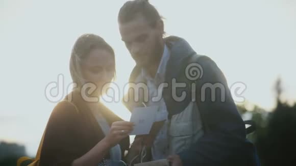 年轻漂亮的夫妇拿着明信片晚上在日落时读些东西男人吻女人的头视频的预览图