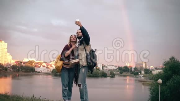 年轻漂亮的夫妇拍自拍照片用智能手机背景上的日落和彩虹视频的预览图