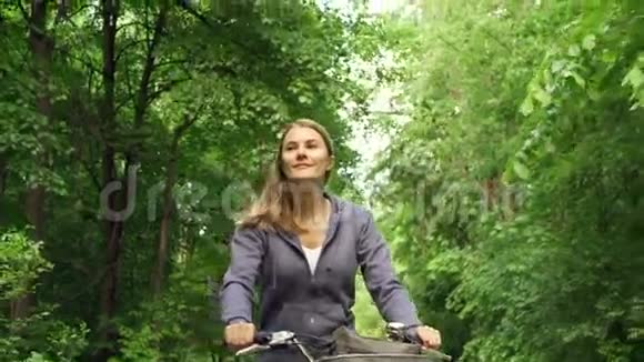 快乐的运动快乐的运动活泼的运动年轻女子骑着帽衫在夏天阳光明媚的公园里骑自行车视频的预览图