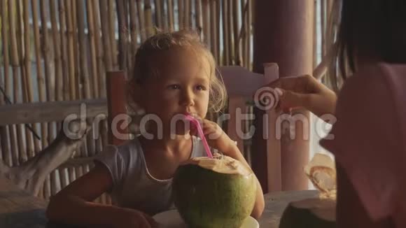 年轻的母亲和女儿坐在海景咖啡馆一起喝椰子视频的预览图