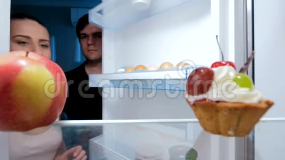 一对年轻夫妇晚上饿了在冰箱里找食物节食的概念视频的预览图