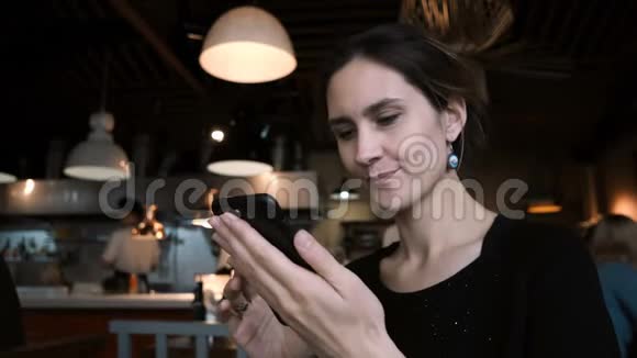 年轻微笑的女人坐在咖啡馆里用智能手机有魅力的女性与朋友在社交网络上聊天视频的预览图
