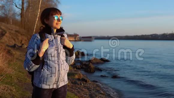 秋天日落时分一位戴太阳镜的女游客站在池塘的岸边视频的预览图