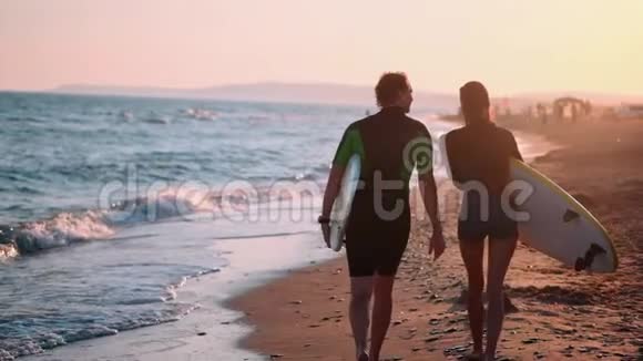 慢动作一对年轻的男女冲浪者穿着湿衣服在海滩上散步手中握着视频的预览图