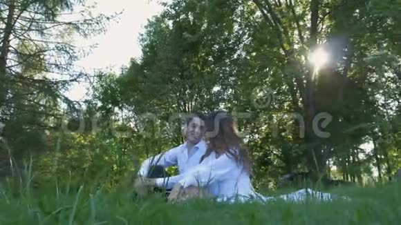 一对美丽的夫妇穿着白色的衣服坐在绿草上浪漫的约会温柔和爱视频的预览图