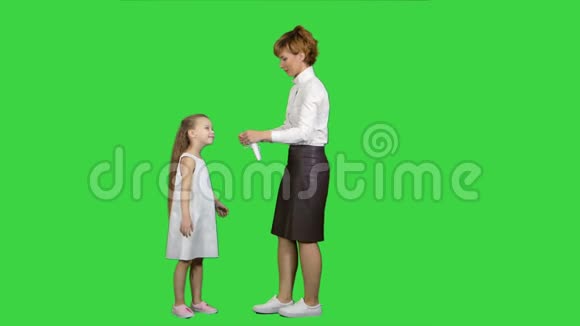 年轻的母亲在绿色的屏幕上给她的小女孩戴上医用面具彩色钥匙视频的预览图
