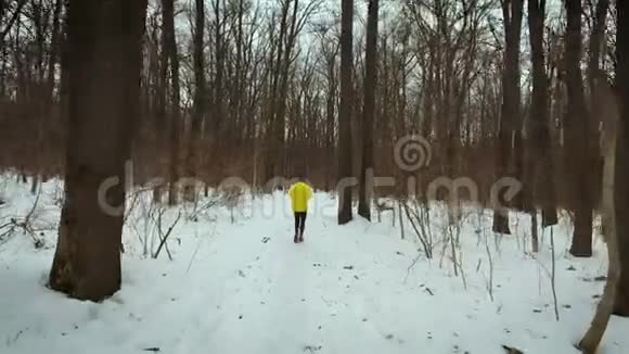 在冬日的白雪覆盖的小路上追踪一个人在森林中奔跑的镜头视频的预览图