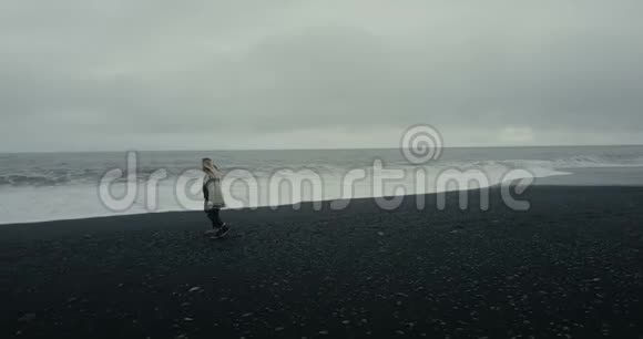 科普特穿着冰岛毛衣在冰岛黑色火山海滩上漫步望着海浪视频的预览图