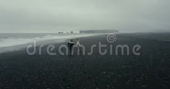 科普特穿着冰岛毛衣在海边奔跑的一对年轻夫妇飞了起来冰岛的黑色火山海滩视频的预览图