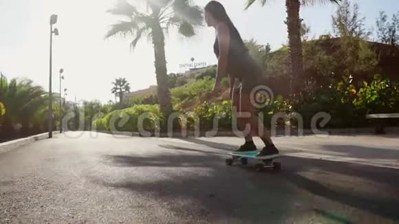 年轻女孩在长板上的棕榈树附近的道路上缓慢地行驶视频的预览图