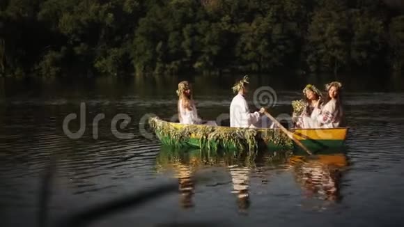 年轻人和三个穿着花环和刺绣衬衫的漂亮女孩漂浮在河上的一艘船上斯拉夫语视频的预览图