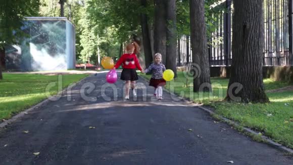两个快乐的小女孩带着气球在绿色的夏日公园散步视频的预览图
