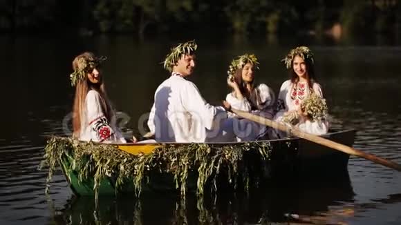 三个女孩和一个男人穿着斯拉夫民族服装漂浮在船上穿花环的女孩坐在船上民族传统视频的预览图