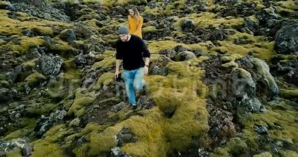 在冰岛火山熔岩里漫步的年轻时尚夫妇的空中景色男人和女人去他们的车视频的预览图
