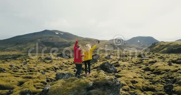 冰岛熔岩场上两个女人站在岩石上的鸟瞰图游客看风景跳舞和跳跃视频的预览图