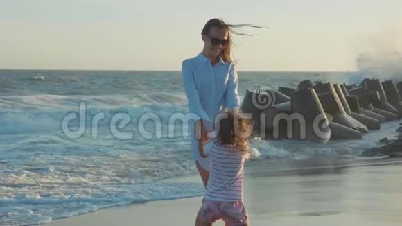 母亲把她的小女儿在温暖的夕阳下在沙滩上旋转视频的预览图