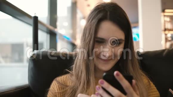 年轻漂亮的女孩坐在咖啡馆的沙发上在网上和朋友聊天微笑着女人用智能手机视频的预览图