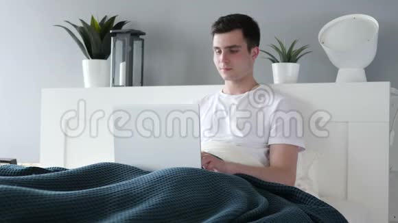 兴奋男子在床上在线视频聊天视频的预览图