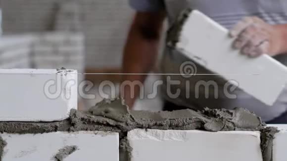 那人用绳子把砖块放在混凝土上为了保持均匀他用一把铲子敲打建筑工人的手视频的预览图