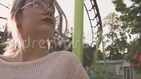戴眼镜的漂亮女孩在大太阳耀斑的过山车附近摆姿势视频的预览图