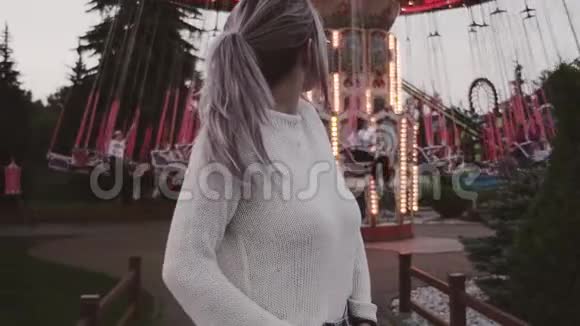 戴眼镜的漂亮女孩站在游乐园的旋转木马附近视频的预览图