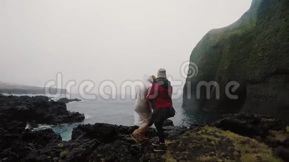 年轻的旅行夫妇站在海边的岩石上一起欣赏美丽的景色视频的预览图