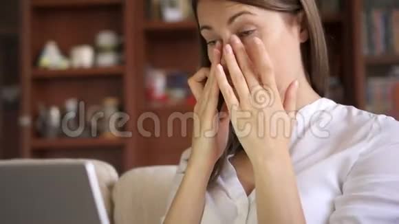 漂亮的疲劳压力过大的女商人在家客厅里用笔记本电脑工作揉揉她的眼睛视频的预览图