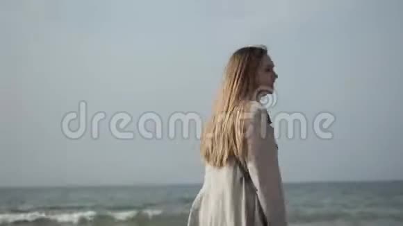 穿着雨衣的年轻女子在海边跳舞沿着海岸散步视频的预览图