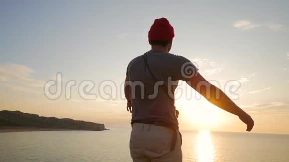 徒步旅行者站在靠近大海的悬崖边举起双手迎接令人惊叹的日落快乐的人到了视频的预览图