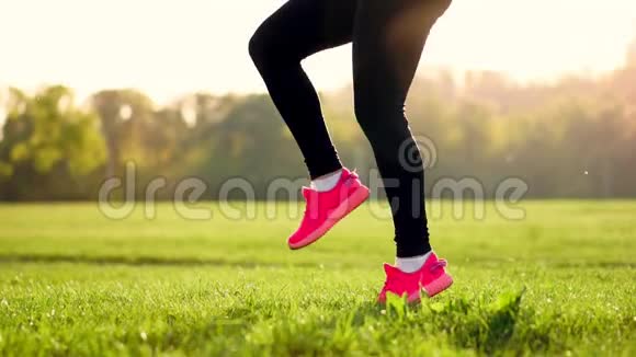 日落时分在草地上一个运动的女孩穿着白色的上衣和粉红色的运动鞋在提起前进行热身运动视频的预览图