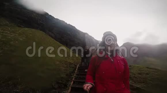 年轻快乐的女人拿着自拍棒和戈普罗从楼梯上下来在山里旅行的夫妇慢节奏视频的预览图
