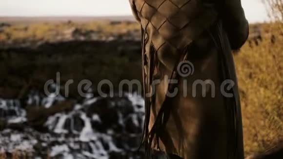 冰岛Barnafoss瀑布前站着的年轻女子的特写后景从风中的夹克波浪中退缩视频的预览图