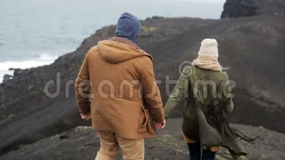 在刮风的日子里年轻夫妇在海边的悬崖上散步牵手在大自然上浪漫的约会视频的预览图