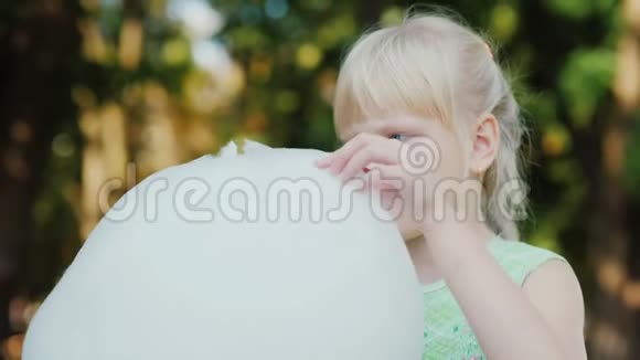 一个金发女孩的肖像在公园里吃甜棉毛晴朗的夏日快乐的假期视频的预览图