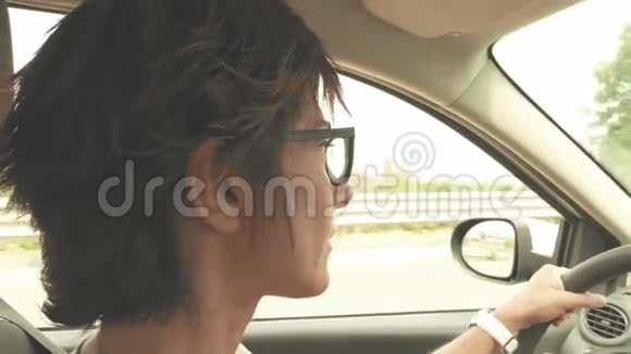 戴眼镜的女人开车双手握在方向盘上室内封闭侧视街道交通老式过滤器t视频的预览图