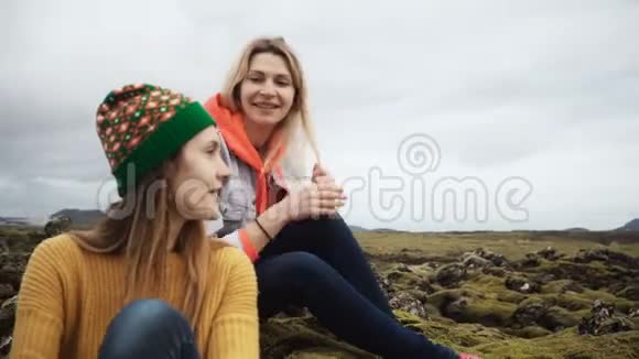 两个幸福的女人坐在熔岩场上覆盖着冰岛的苔藓聊天游客朋友徒步旅行后休息视频的预览图