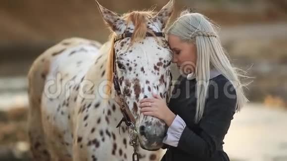 年轻的金发女人抚摸和拥抱马美丽的女士和她的白色种马在海滨享受自然爱和爱视频的预览图